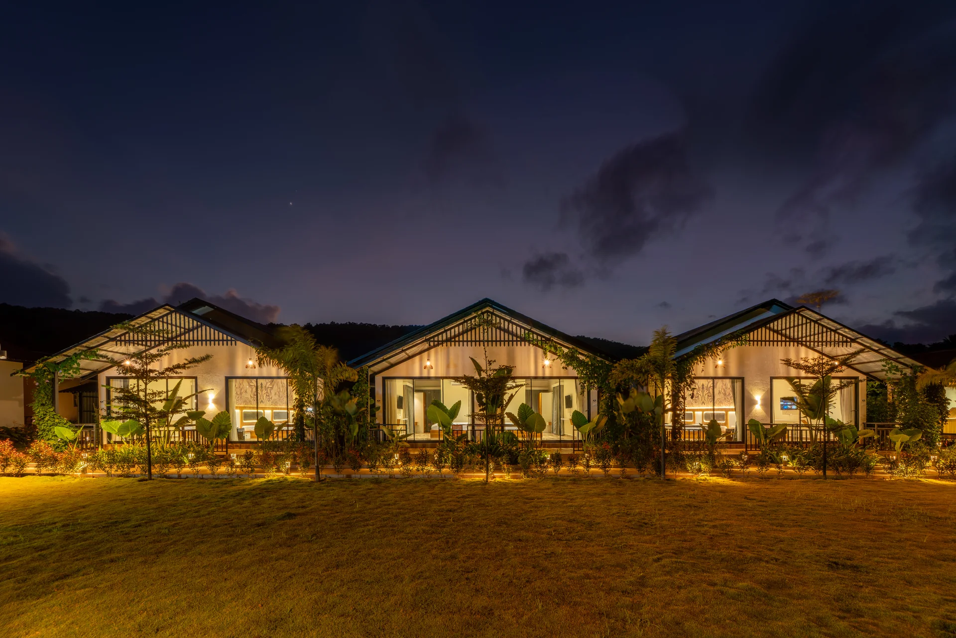 Cottages across the lawn at night at Nadi Teera, Dandeli
